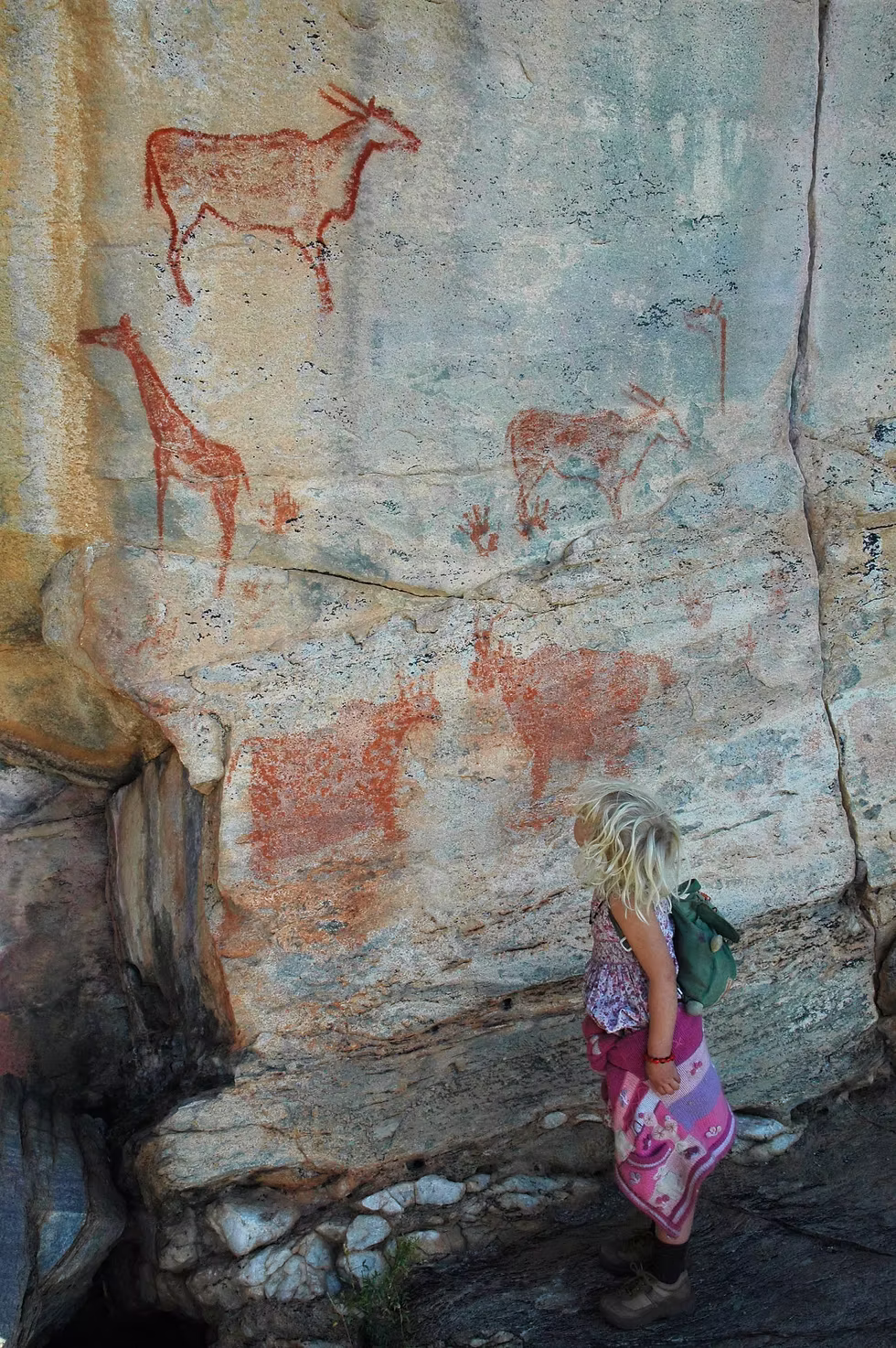 My daughter, then 4 years old, stands by a group of paintings, showing an eland at the top, a giraffe on the left, and, if you look closely, a handprint in the middle, Tsodilo Hills. Photo: Jessica Groenendijk